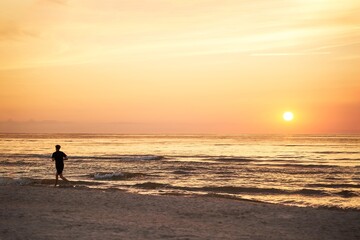Silhouette of a sportsman running near the ocean shore at sunset.