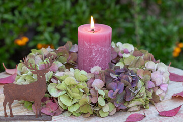 Arrangement mit einer Kerze und Blumenkranz mit Hortensienblüten