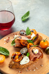 bruschetta with prosciutto, cherry tomatoes and cream cheese with basil leaves, antipasto wine. place for text, top view