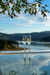 Two glasses of champagne on the edge of the pool against the background of mountains, lake, blue sky with clouds
