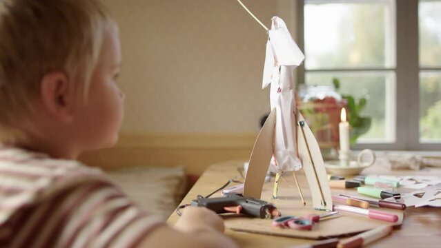 Young caucasian boy admiring his paper rocket science experiment indoors