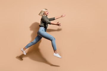 Fototapeta na wymiar Full length photo of cheerful excited lady wear khaki shirt jumping high running fast empty space isolated beige color background