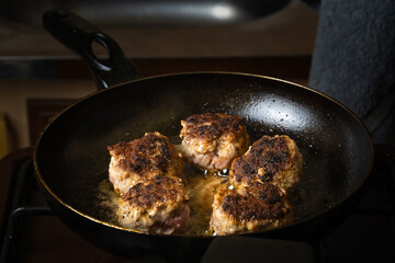 Close-up of fried minced meat cutlets in a frying pan. Cook turns the cutlets in the pan with a fork. Russian or Polish version of cutlets - kotlety.