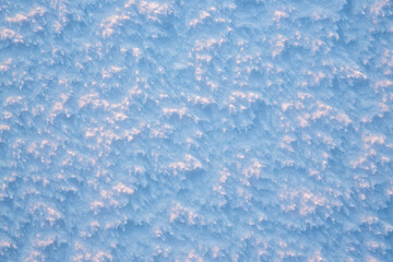 Fototapeta na wymiar Natural snow texture. The surface of an icy snow crust. Snowy ground. Winter background with snow patterns. Perfect for Christmas and New Year design. Closeup top view.