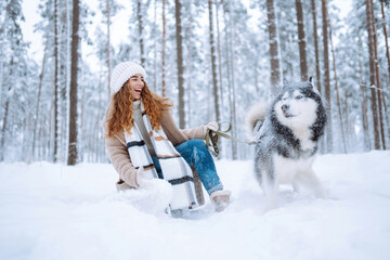 Beautiful young woman plays with her dog in the winter forest. First snow. Friendship, love and devotion concept. Outdoor recreation