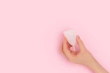 Female hand hold white menstrual cup on a pink background. Minimal concept with copy space. - obrazy, fototapety, plakaty
