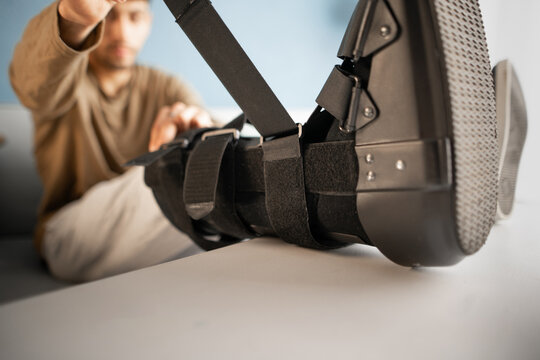 Close-up of an injured man putting on an ankle brace while sitting on a sofa