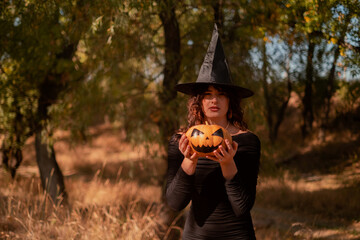 Beautiful woman in witch costume with Jack-o'-lantern in forest, Halloween party, smiling evil...