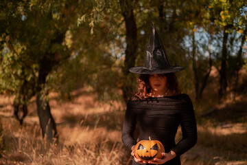 Beautiful woman in witch costume with Jack-o'-lantern in forest, Halloween party, smiling evil...