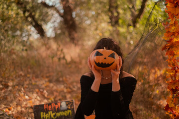 Beautiful woman in witch costume with Jack-o'-lantern in forest, Halloween party, smiling evil...