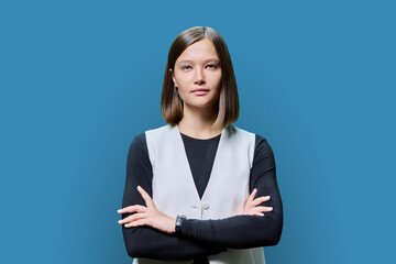 Serious confident young woman with crossed arms posing against blue background
