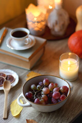 Cup of tea or coffee, plate with desserts, dried oranges, bowl of grapes, scented candles, vintage books, pumpkins and autumn leaves on the table. Autumnal hygge. Selective focus.