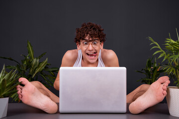 A funny young man sits at a laptop with his feet up on the table. Watching videos for adults....