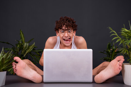 A funny young man sits at a laptop with his feet up on the table. Watching videos for adults. Dating on the Internet.