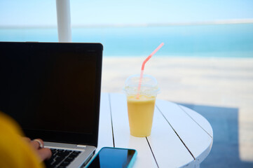 Selective focus. Partial view laptop and smart mobile phone with mockup digital screen and glass of fresh fruit smoothie