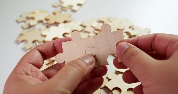 Jigsaw Puzzle pieces on the table then the lefthand and the righthand put two pieces together making them fit before laying on the table.