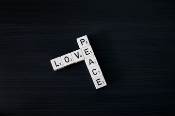 Peace and Love being spelled out by wooden word dice above a dark wooden effect background