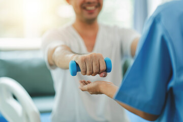 Physical therapist giving exercise by maintaining dumbbells on the arms and shoulders of a male...