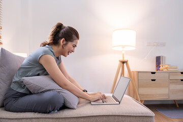 Young woman asian using laptop pc computer on couch relax surfing the net at home