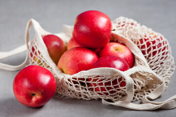 Seasonal red apples in a string bag on a gray background in a eco-friendly bag