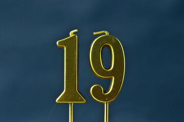 close up on the gold number nineteen candle on a dark background.
