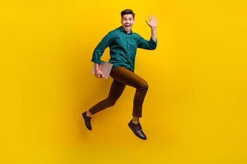 Fototapeta na wymiar Photo of glad friendly man wearing trendy clothes carrying modern device running work waving arm isolated on yellow color background