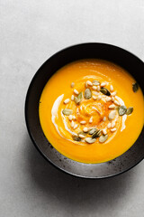 Seasonal autumn food. Pumpkin soup with cream, croutons and pumpkin seeds in a black plate on a gray background. Top view, copy space, minimalist