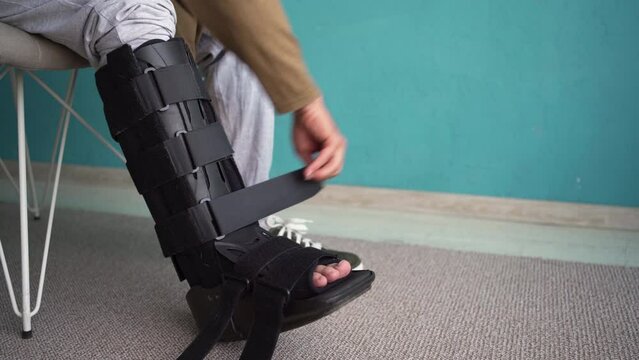 A man removing an ankle orthosis sits on a chair at home