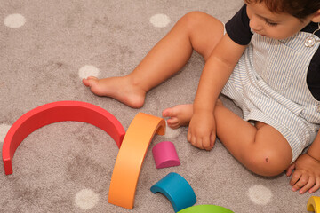 Toddler playing on the carpet with a wooden rainbow