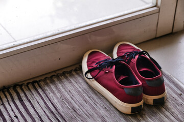 Pair of dark red sneakers on a mat, near entrance glass door