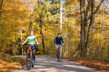 Young happy couple cycling downhill along the autumn forest trail, holding hands and having fun in...