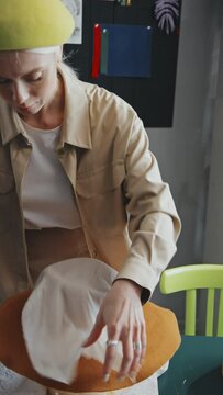 Vertical shot of Caucasian female hat-maker ironing new felt hat through white cloth