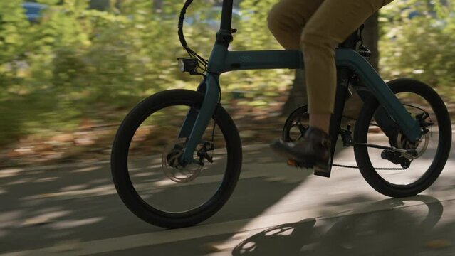 Stylish young woman riding an electric bicycle in city centre in modern street during fall season. Close up view of woman pedalling with boots, wheel rotation view