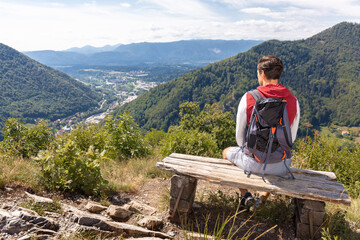 Hiking man sitting on a bench at a viewpoint enjoying beautiful mountains and valley landscape
