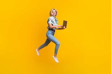 Full size photo of smart clever girl wear print blouse jeans flying run empty space with laptop isolated on yellow color background
