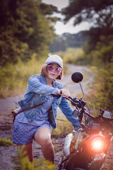 beautiful woman wearing blue jeans jacket sitting on enduro motorcycle against colorful natural  background