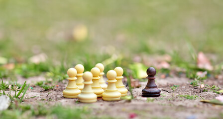 Symbol for excluding someone who is different. A group of white chess figueres is seperated from a single black figure.
