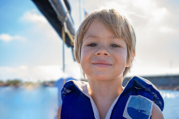 Happy boy wearing lifejacket and enjoying fresh air while standing looking away holding on metal...