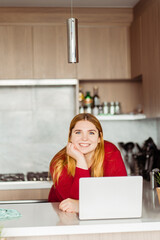 Portrait of smiling plus size woman using laptop, working at home in kitchen in cozy apartment