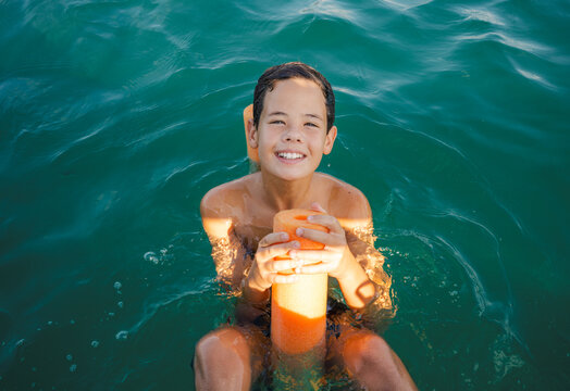 Handsome teeneger boy swimming with a float in the sea on a hot summer day