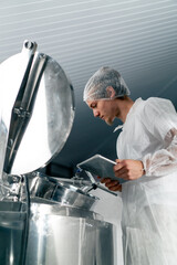 Close-up shot of a professional technologist with a tablet at food factory opening a tank to...