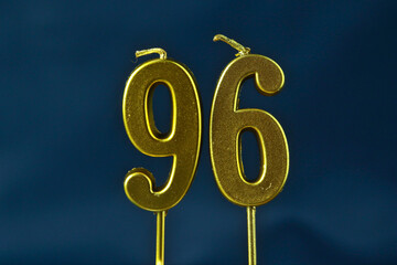 close up on gold number ninety-sixth birthday candle on a dark background.
