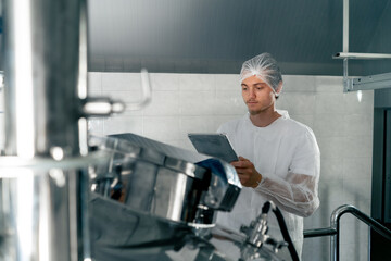 Professional technologist in uniform with tablet at winery opens tank to check fermentation stage