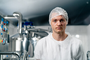 Portrait of a serious technologist in a special uniform standing at a brewery with his arms crossed over his chest and looking at camera
