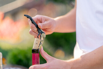 Close-up shot of a male sommelier's hand using a corkscrew to unscrew the wooden cork of wine bottle