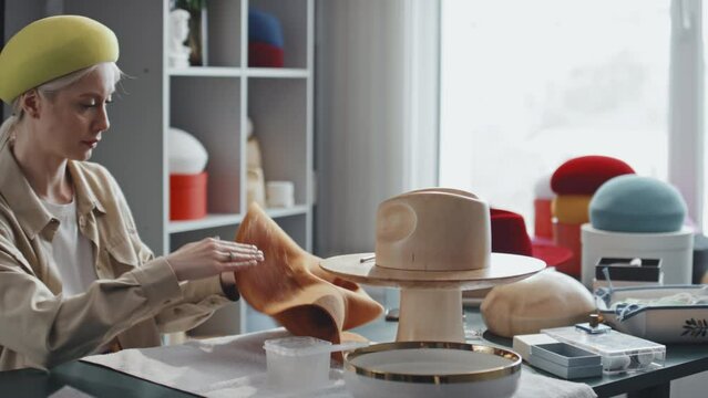 Medium shot of young female hatter having good time while coating new hat with felt stiffener using her hand