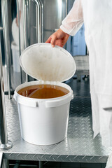 The hand of a technologist opens a barrel of natural liquid honey to be added to production of...
