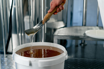 Close-up shot of a metal spoon stirring natural liquid honey which flows back into large bowl