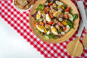 Bowl with vegetable salad on a checkered tablecloth. There are special devices for mixing.
