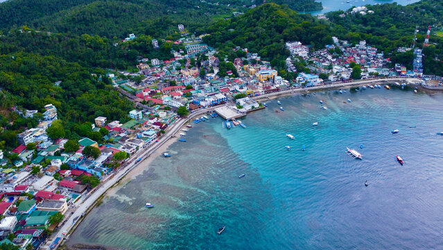 Aerial view of a small town on the shore of a lagoon on a tropical island. Small town, bay, lagoon, boats in the port. Sabang, Puerto Galera, Oriental Mindoro, Philippines.